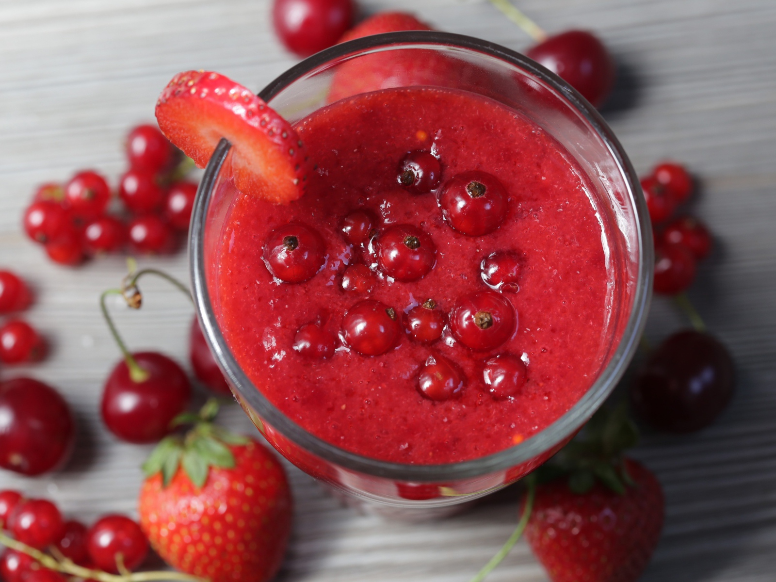 Смузи в стакане с ягодами клубники, красной смородины и вишни