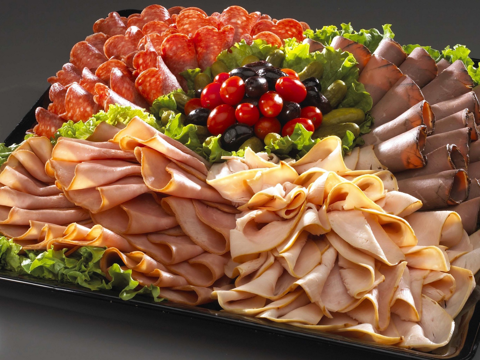 Большое блюдо с аппетитной мясной нарезкой, листьями салата и оливками