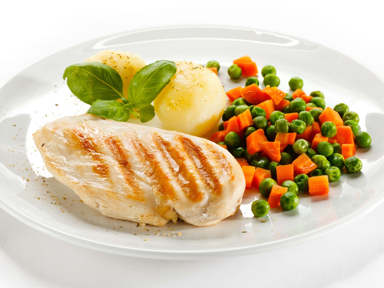 Куриная грудка на белой тарелке с картофелем, морковью и зеленым горошком