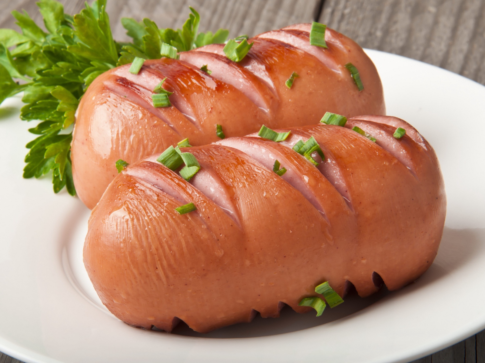 Два жареные сардельки на большой белой тарелке с зеленью 