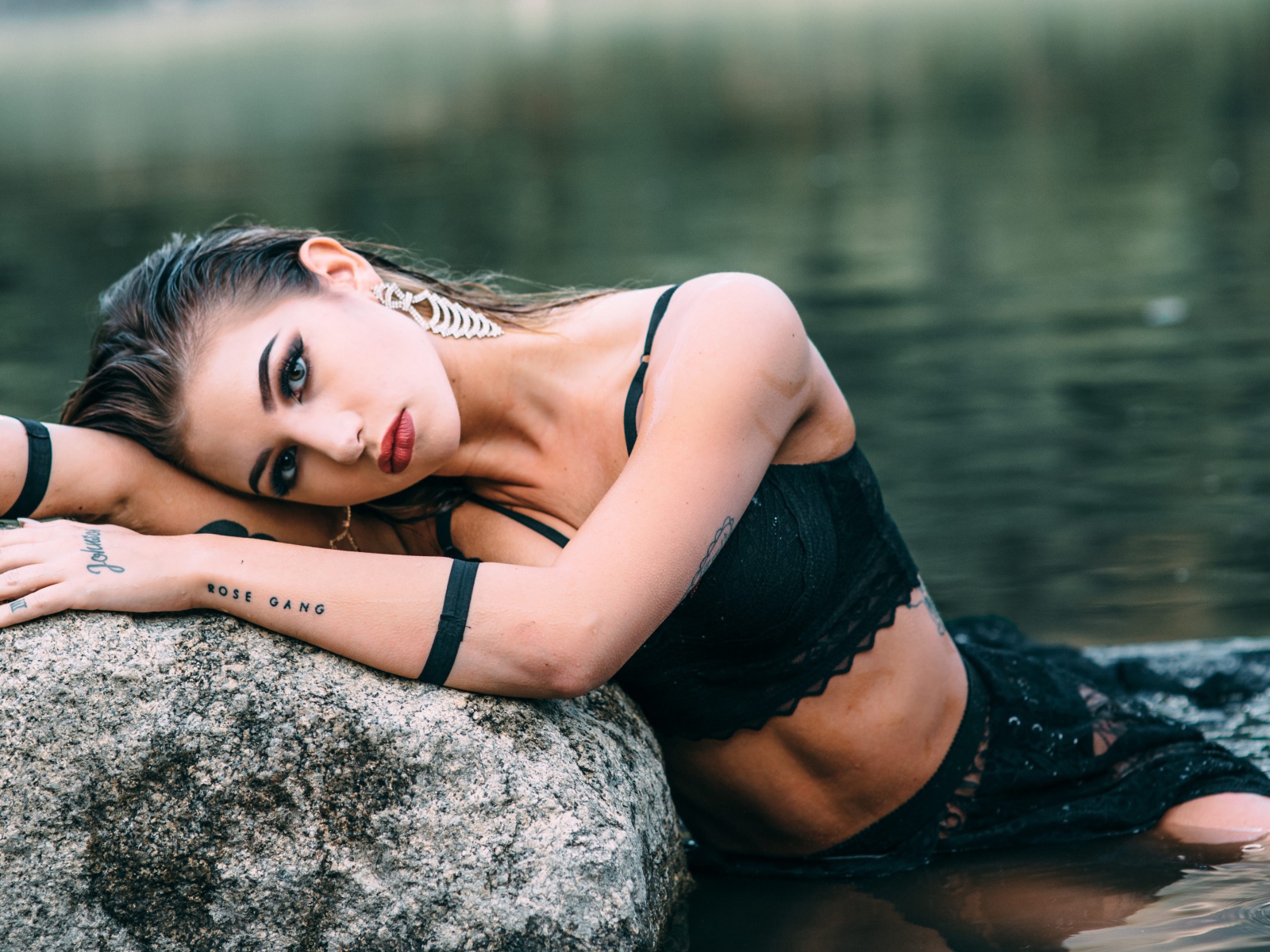 Молодая девушка с татуировками сидит у камня в воде
