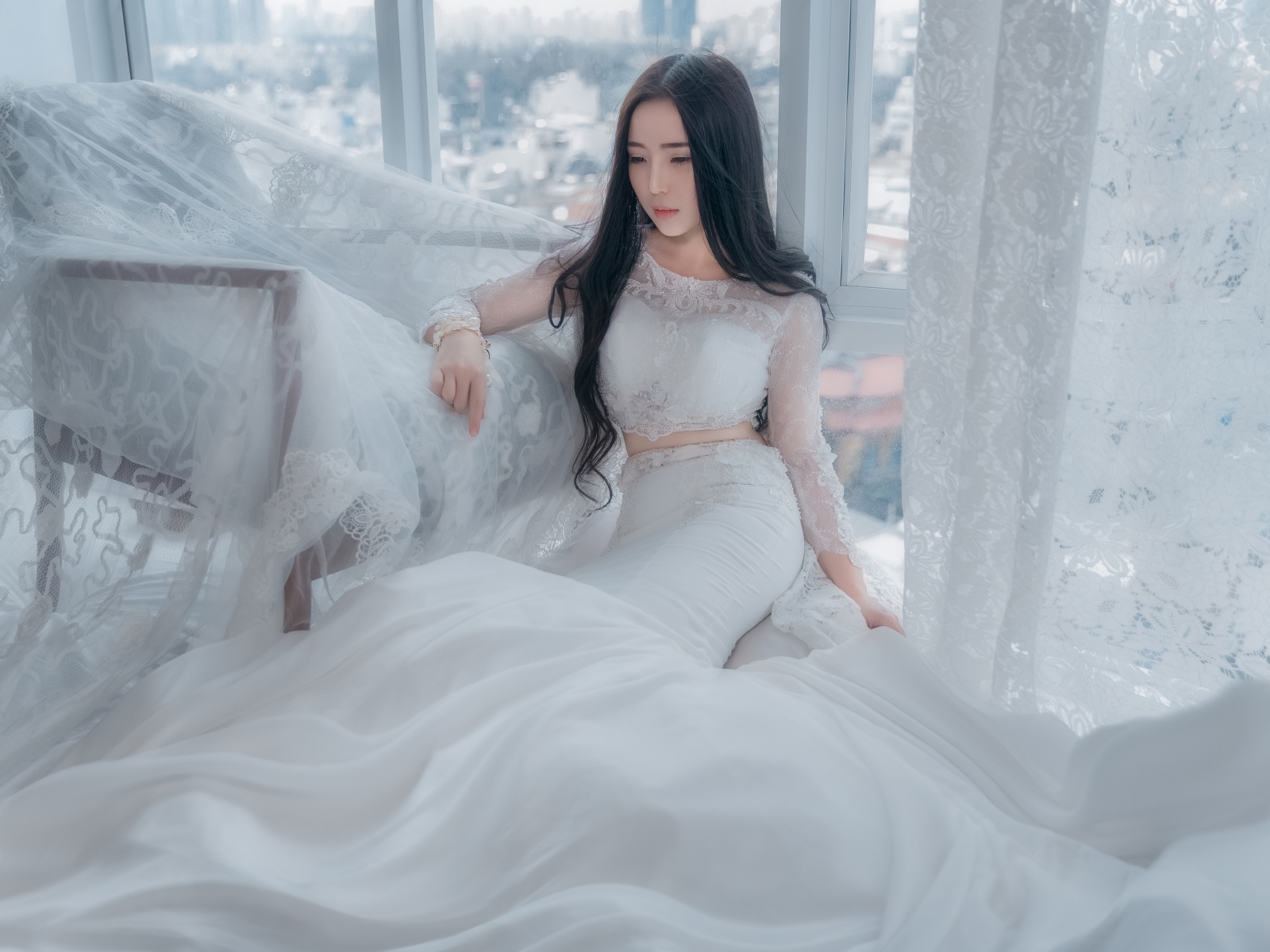 Красивая азиатка в белом свадебном платье сидит на полу