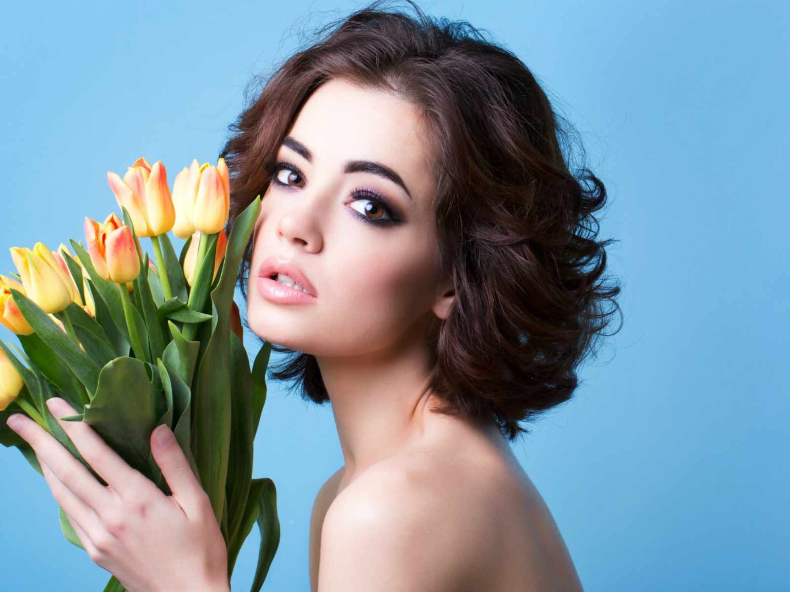 Красивая девушка брюнетка с букетом тюльпанов на голубом фоне
