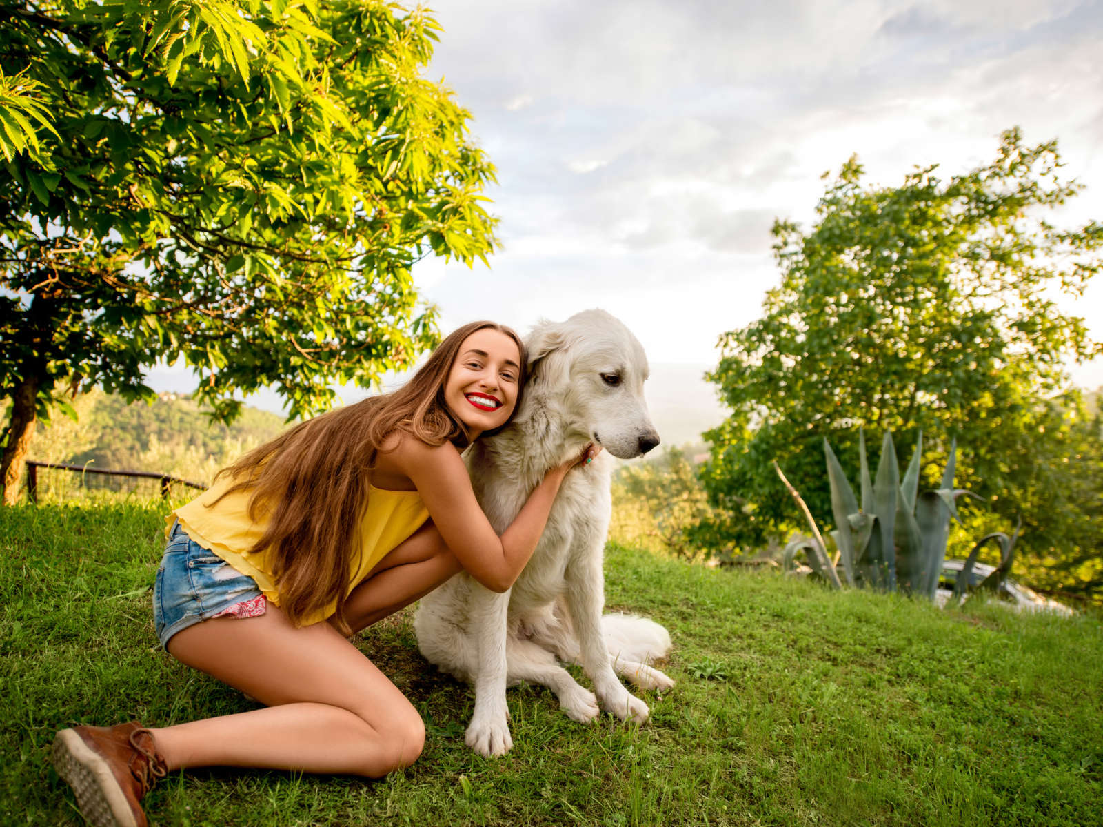 Улыбающаяся шатенка с золотистым ретривером на зеленой траве летом