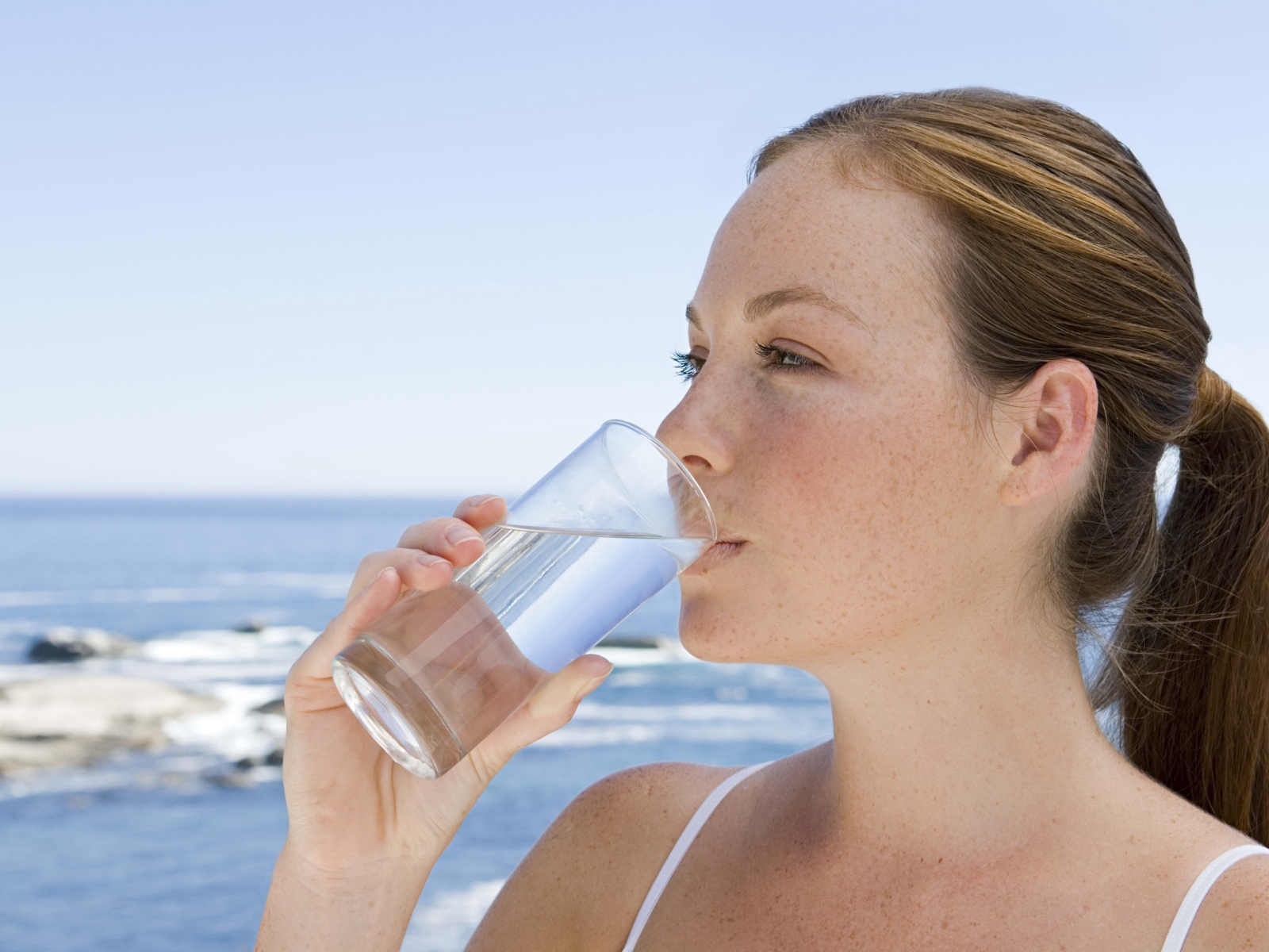 Девушка пьет воду со стакана на фоне моря