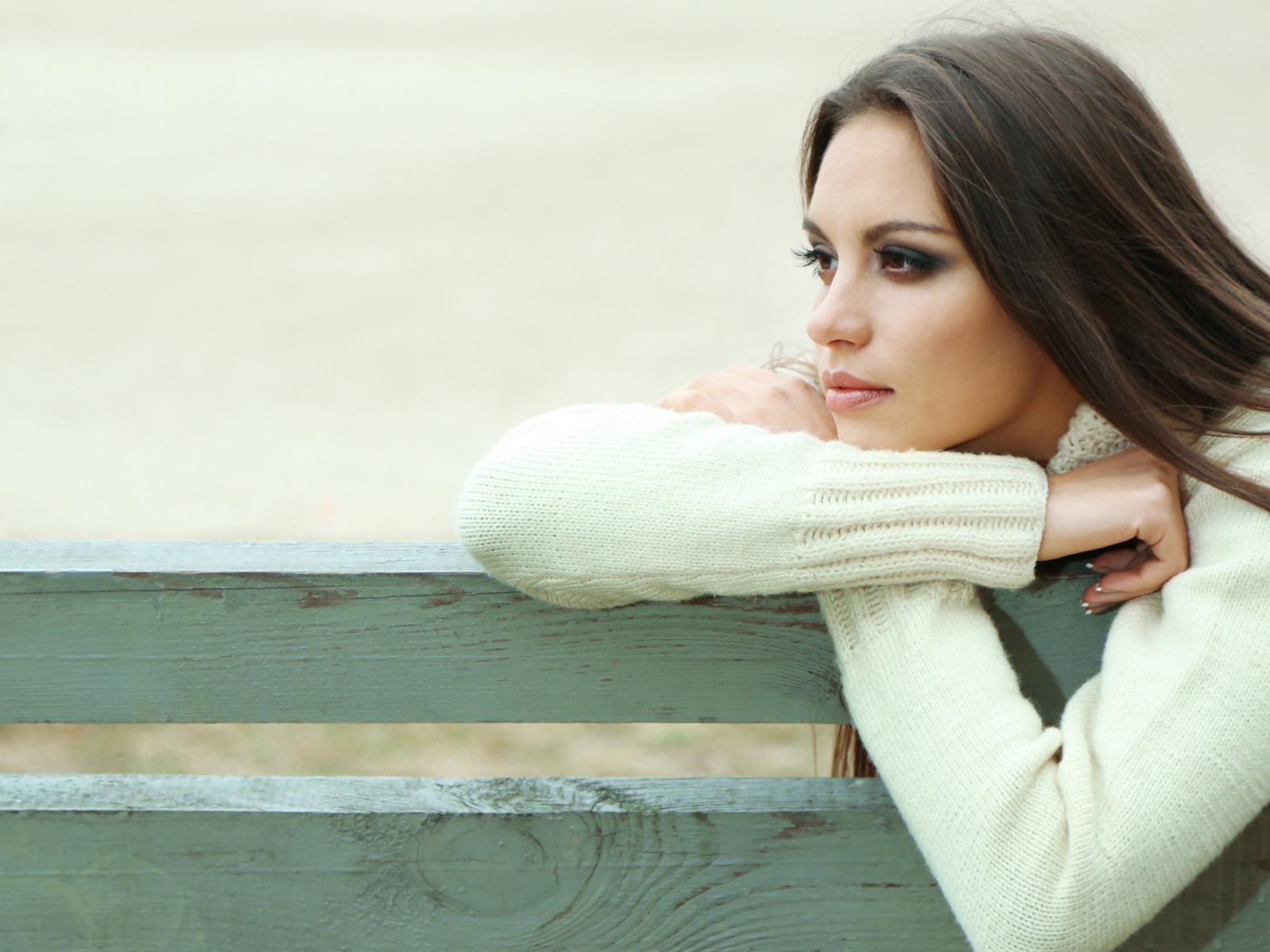 Задумчивая девушка брюнетка в белом свитере сидит на лавке