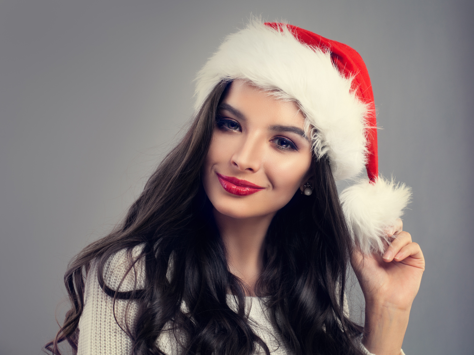 Красивая длинноволосая девушка брюнетка в шапке деда Мороза на сером фоне