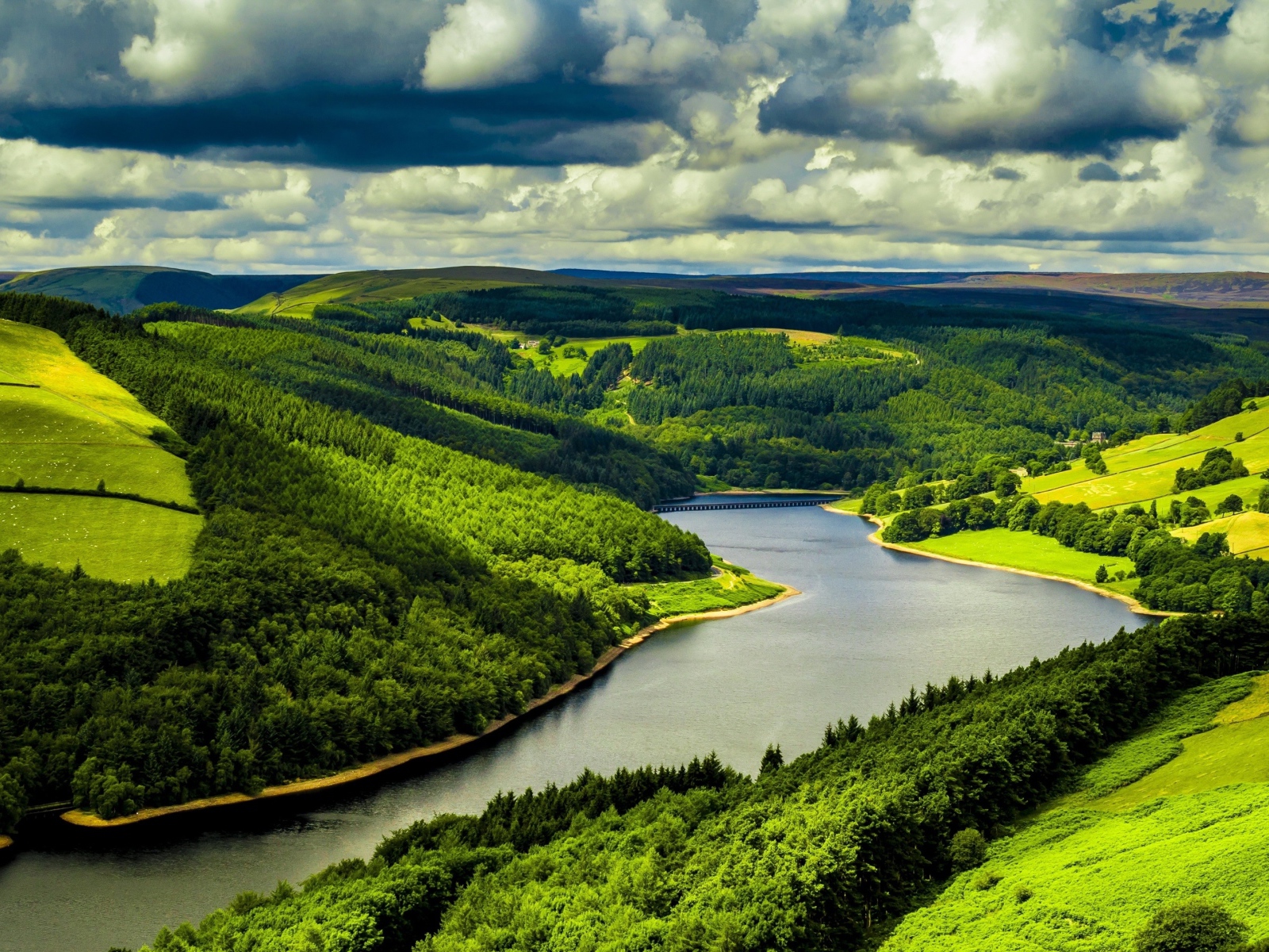 Зеленые холмы у реки под небом с густыми белыми облаками