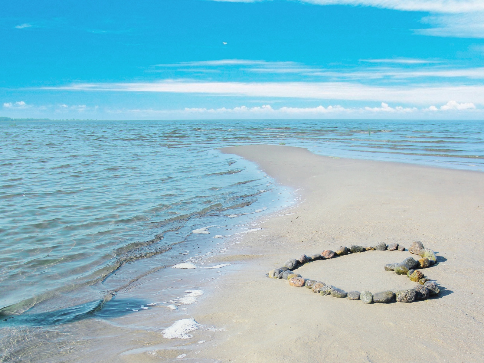 Сердце из камней на песке у спокойного моря под голубым небом