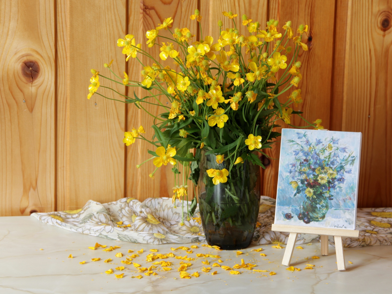 Букет желтых полевых лютиков в стеклянной вазе на столе с картиной