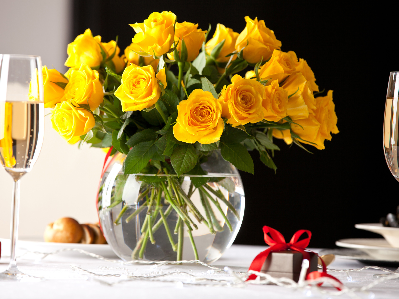 Букет желтых роз в стеклянной вазе с бокалами шампанского на столе