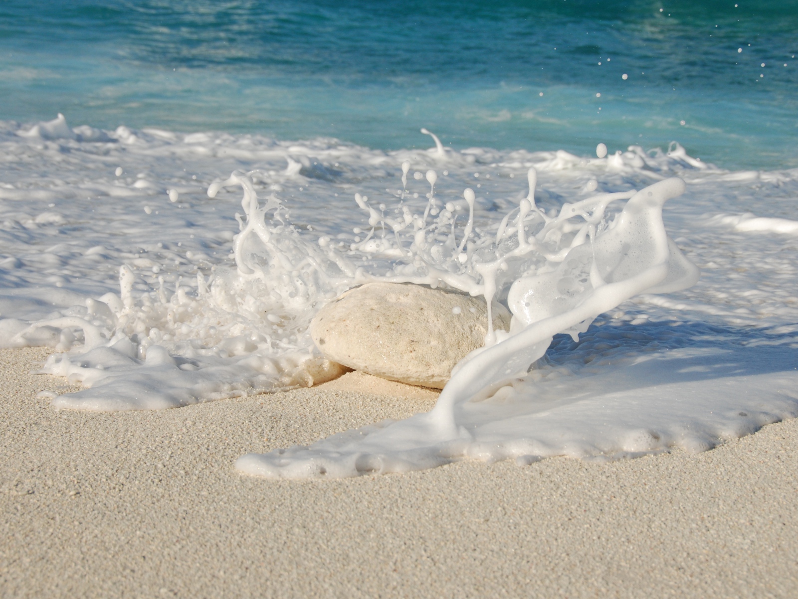 Белые морские волны бьются об камень на желтом песке