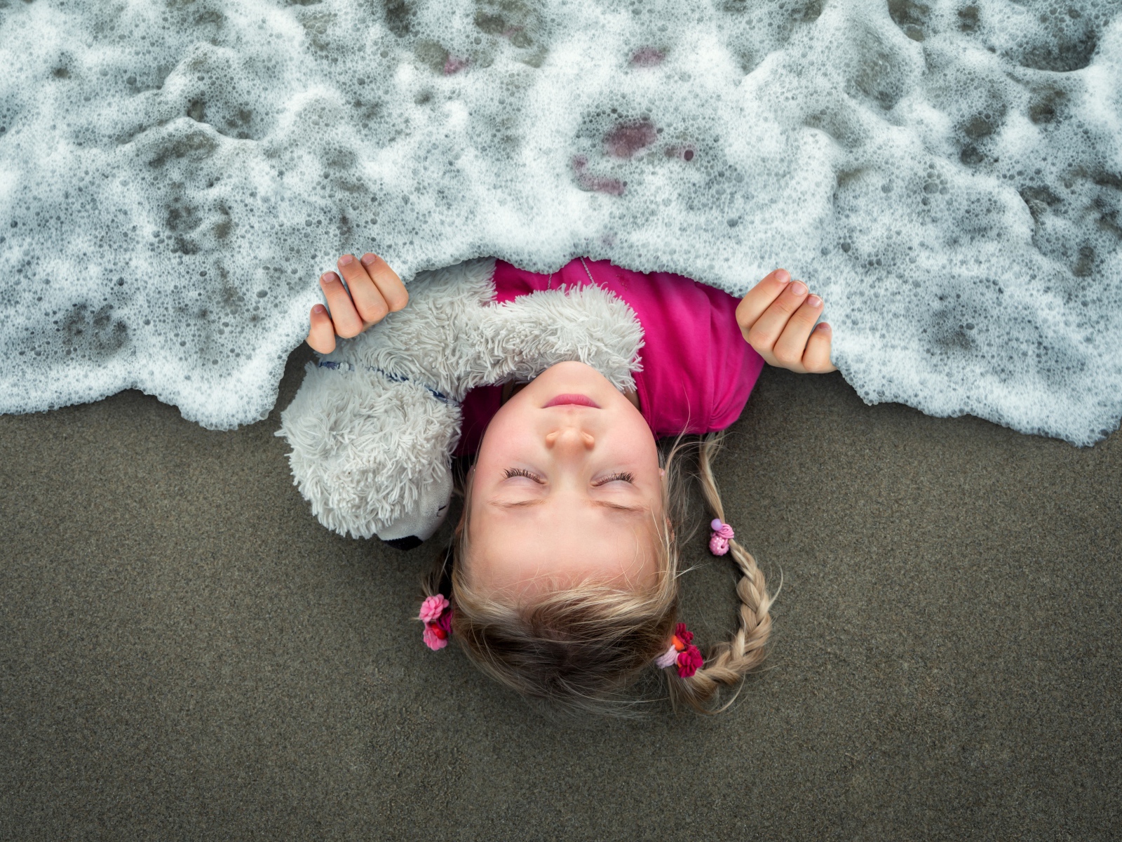 Маленькая девочка спит на песке под одеялом из морской пены