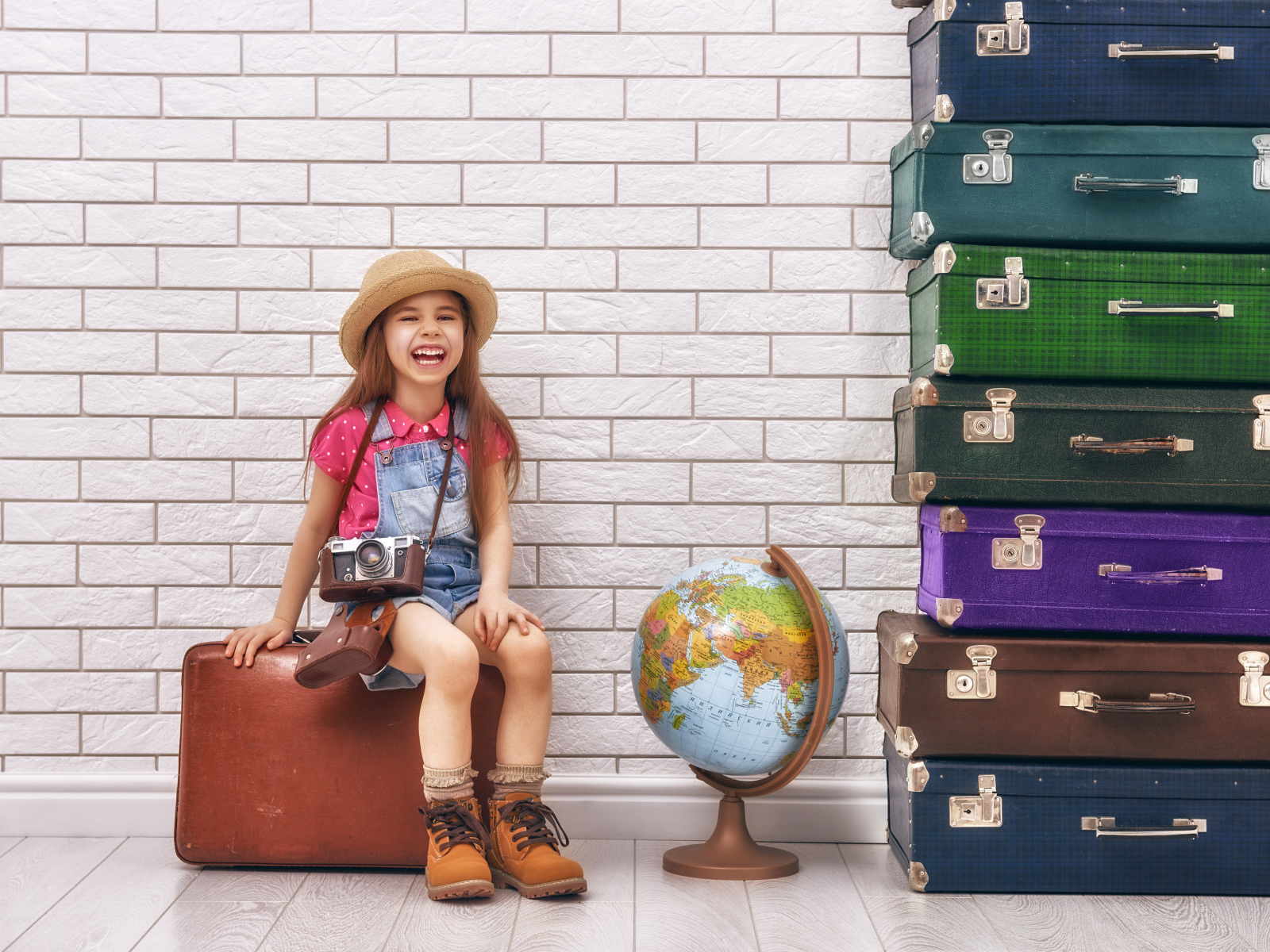 Маленькая девочка с фотоаппаратом сидит на чемодане