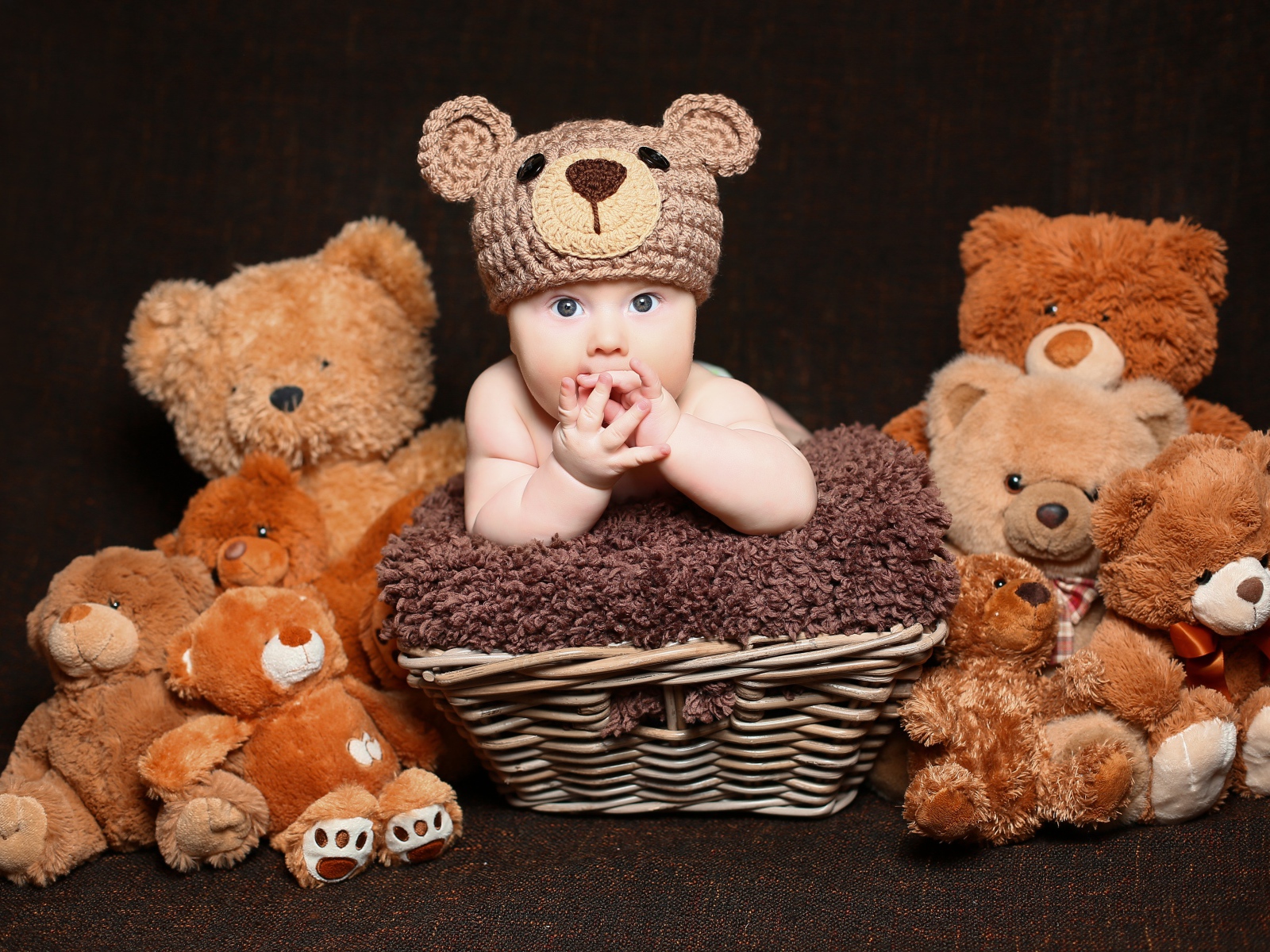 Маленький ребенок в вязанной шапке с  игрушечными медвежатами 