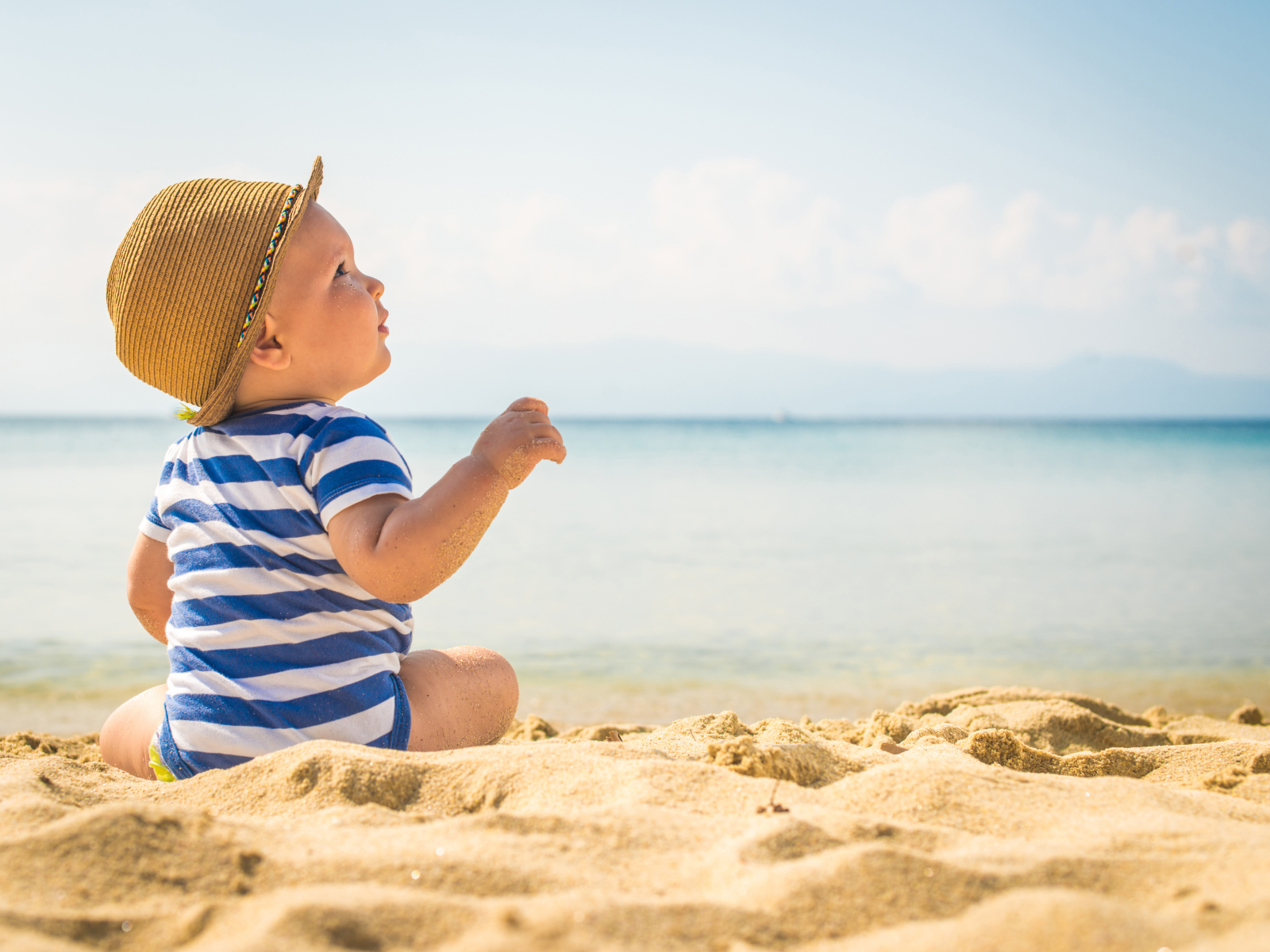 Маленький ребенок сидит на песке на пляже у моря