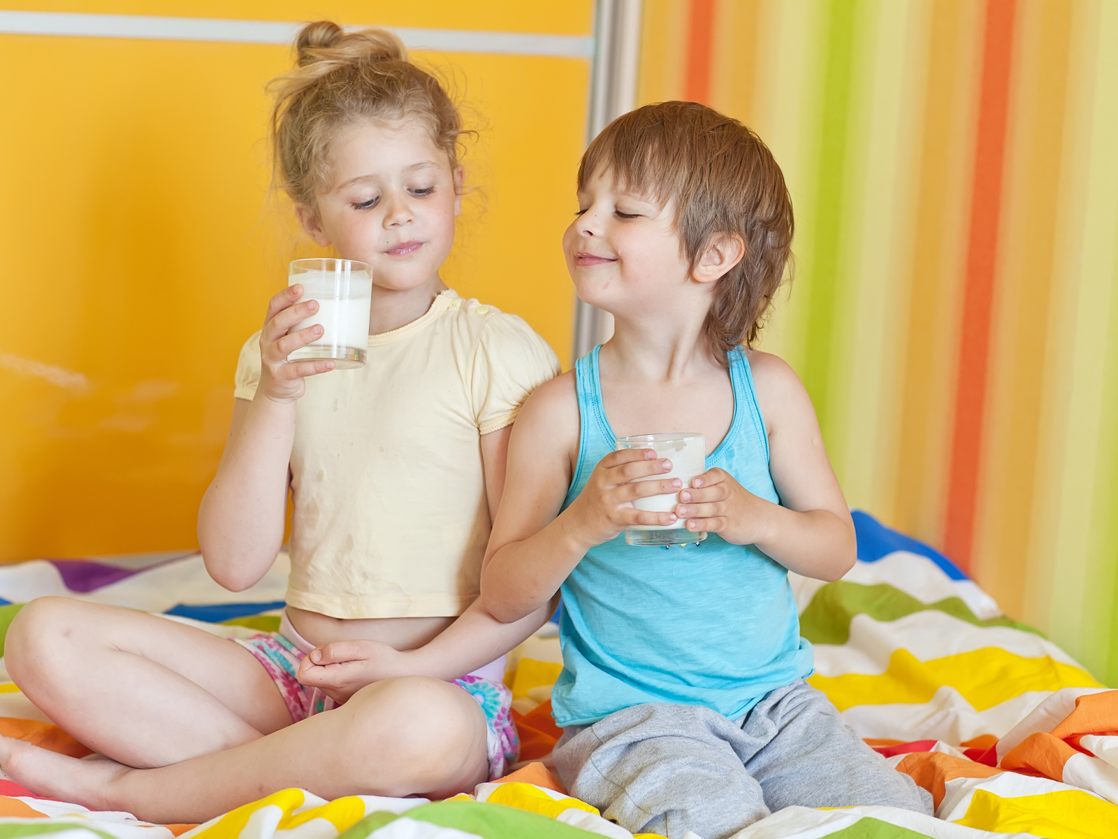 Маленькие мальчик и девочка со стаканами молока в руках 