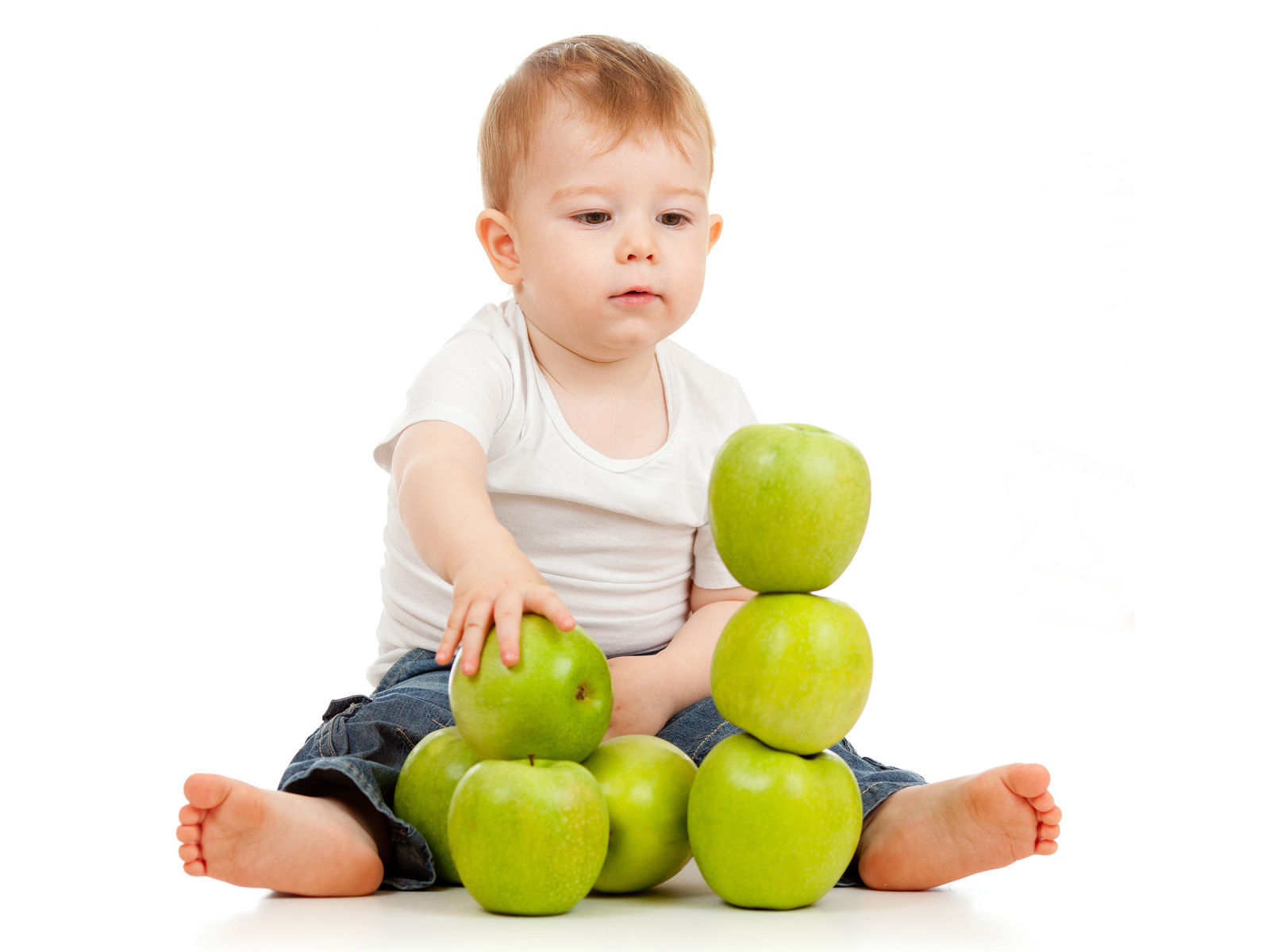 Маленький мальчик играет с зелеными яблоками на белом фоне