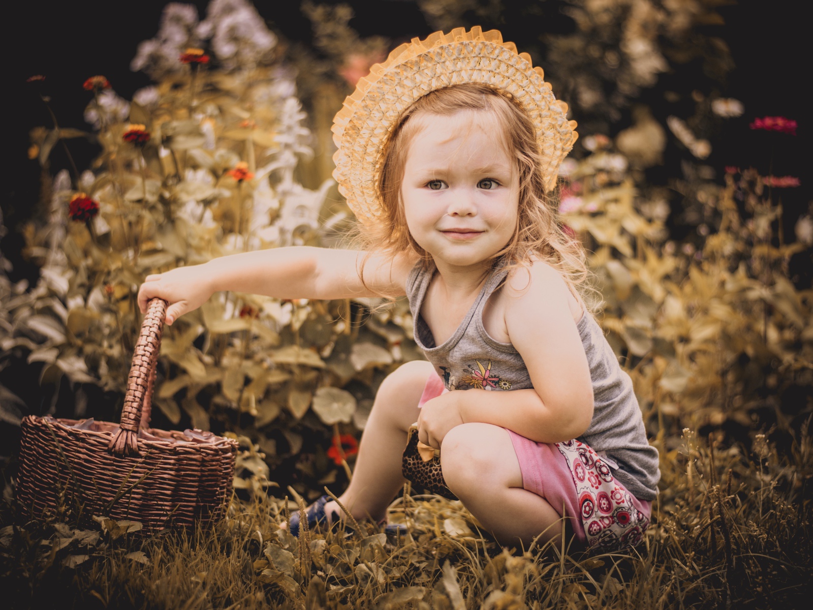 Маленькая девочка в шляпе сидит на траве с корзиной