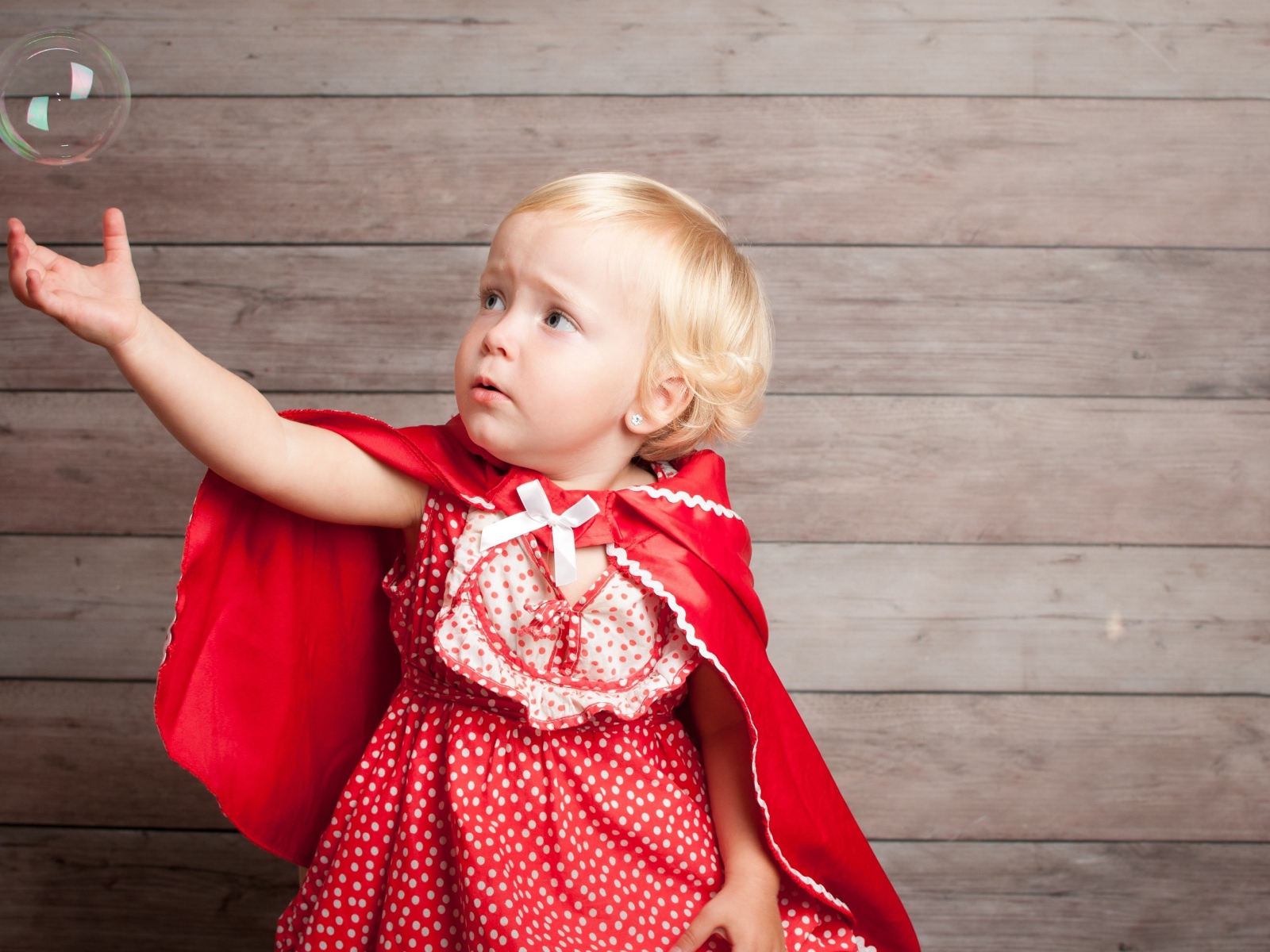 Маленькая девочка в красном платье ловит мыльный пузырь