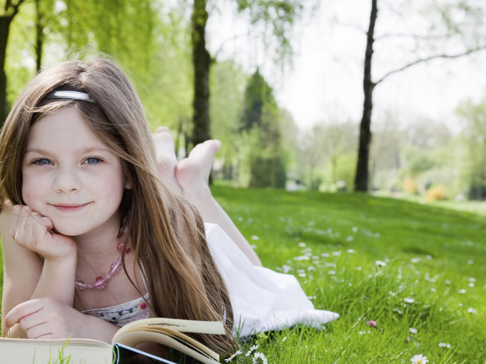 Маленькая девочка с книгой лежит на зеленой траве
