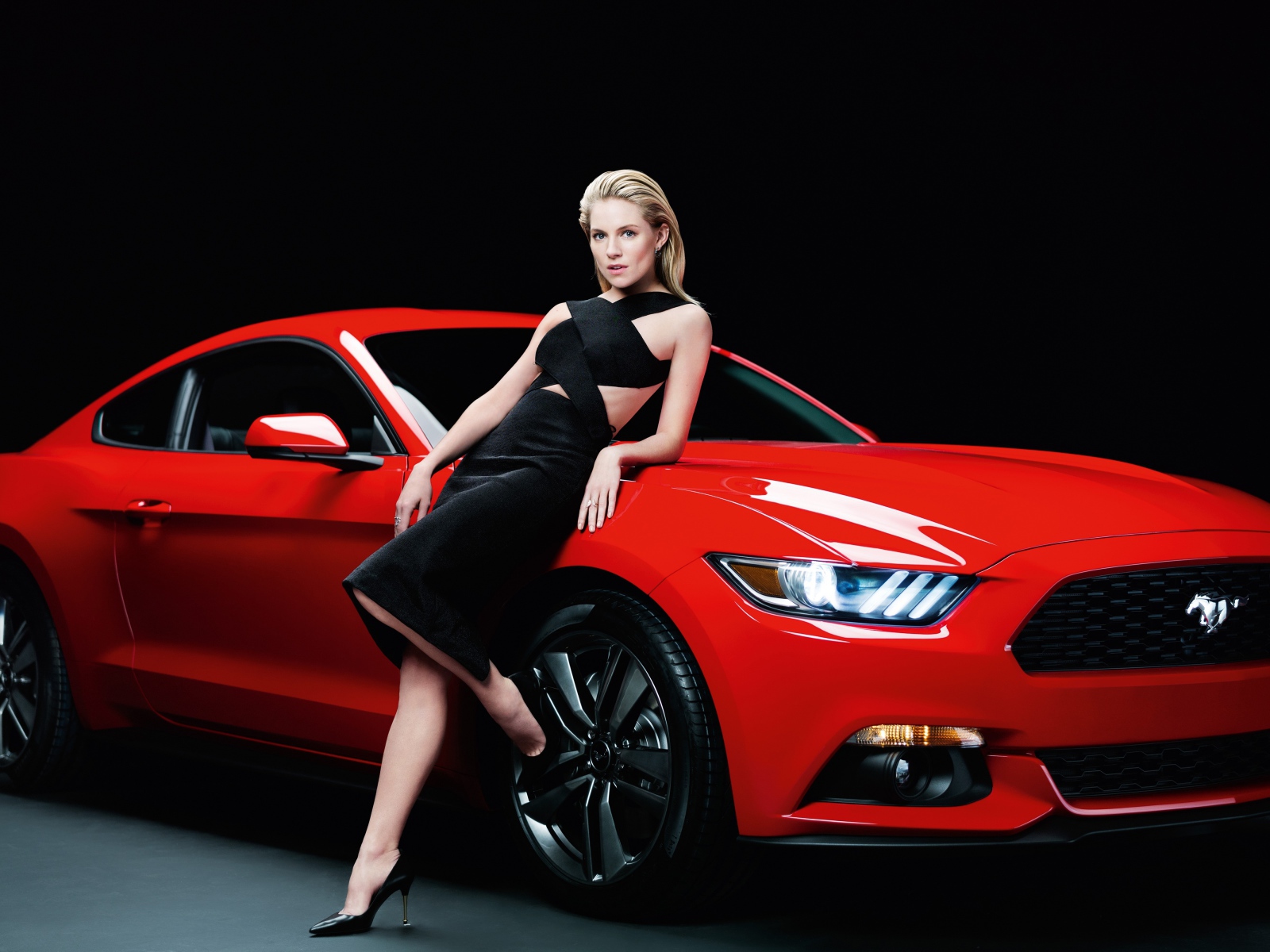 Актриса Сиенна Миллер в черном платье у красного автомобиля Ford Mustang
