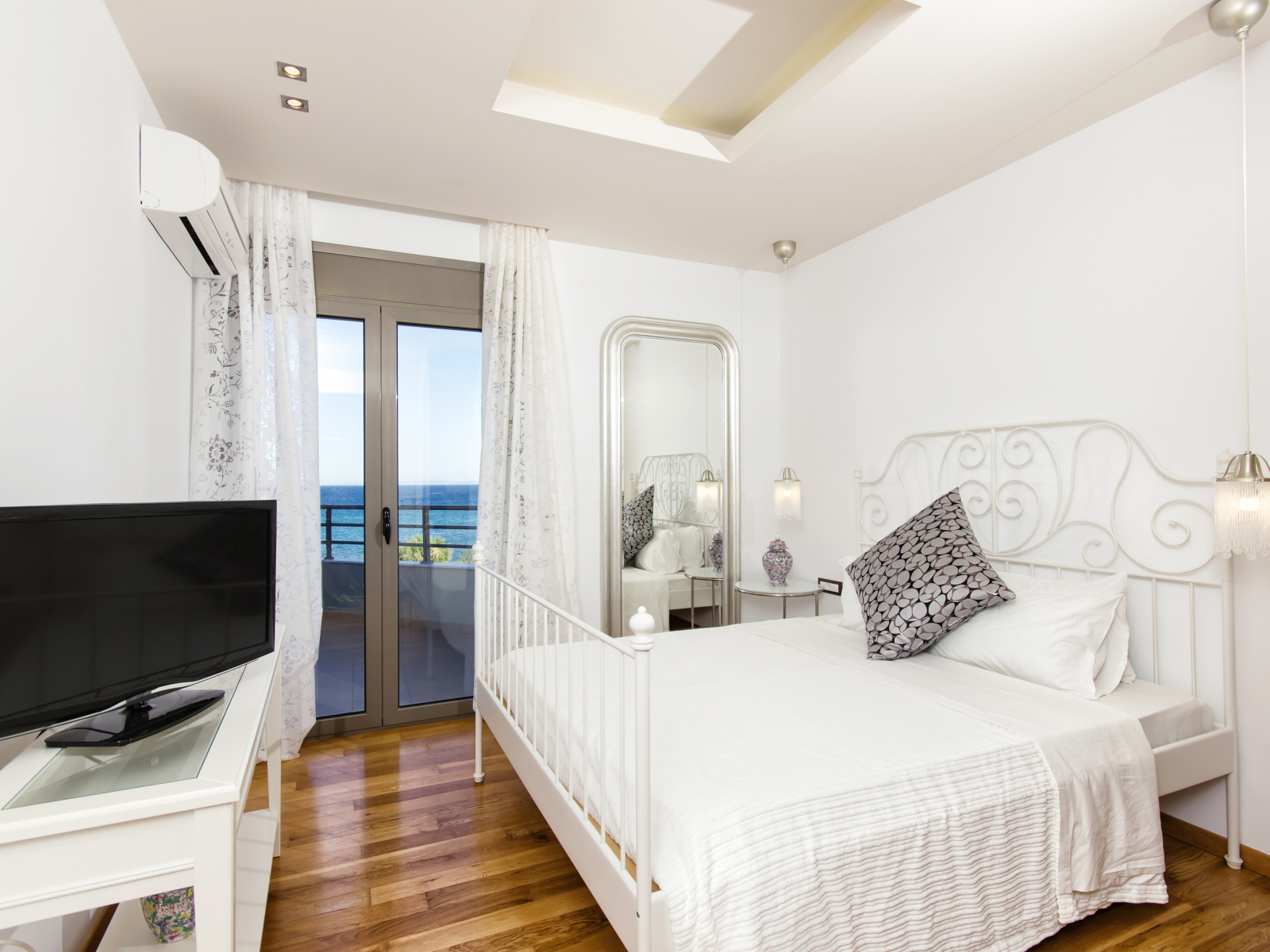 Светлая спальня с большой белой кроватью и телевизором 