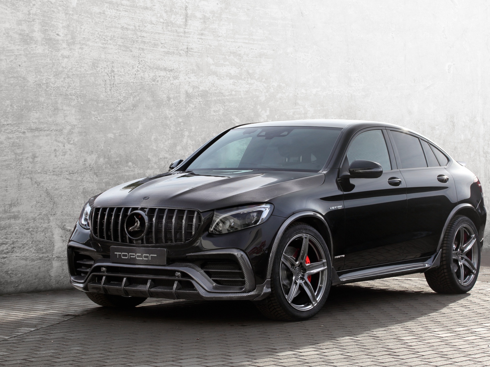 Черный автомобиль Mercedes-AMG GLC 63 на фоне серой стены 