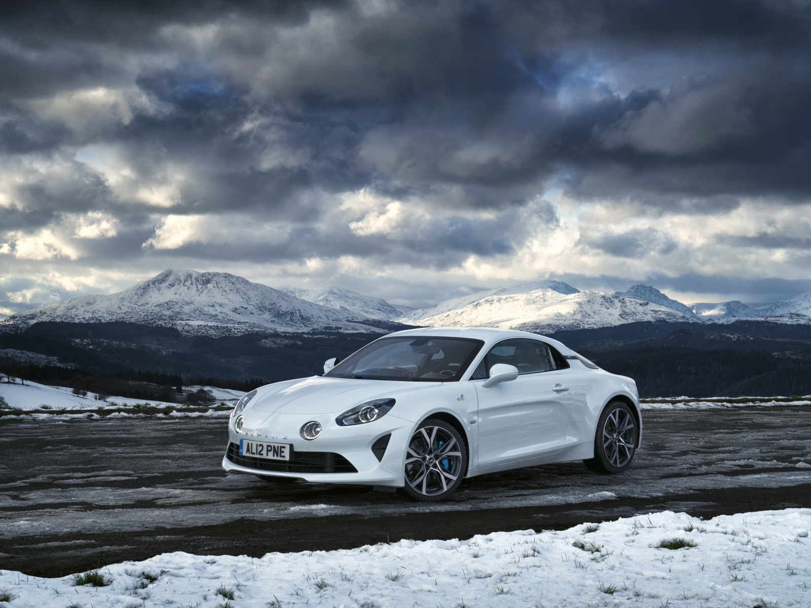 Белый автомобиль Alpine A110 на фоне гор под грозовым небом  