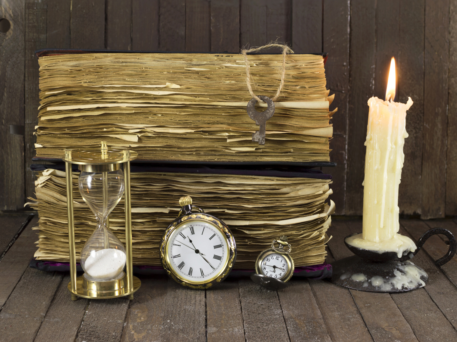 Старинные книги, зажженная свеча, ключи и часы на столе