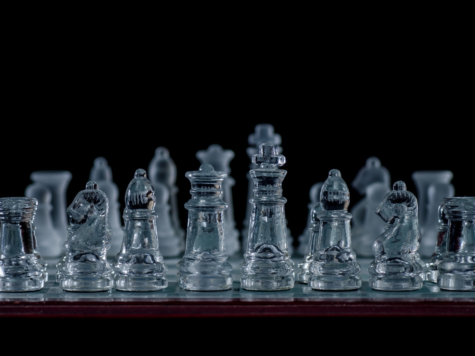 Стеклянные шахматы на доске на черном фоне