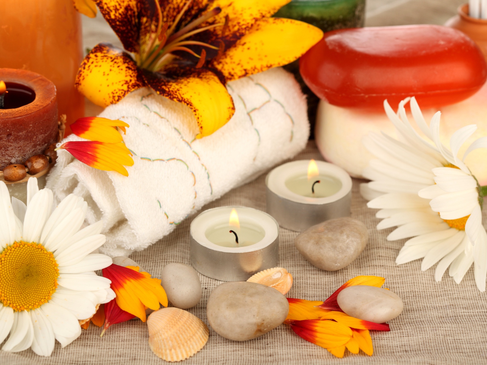 Зажженные свечи на столе с полотенцем, цветами и мылом