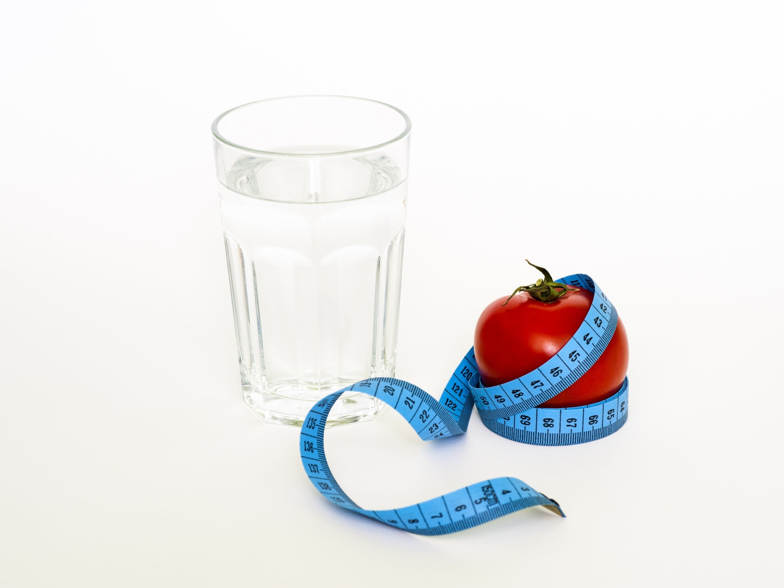 Стакан воды на белом фоне с красным помидором и сантиметром