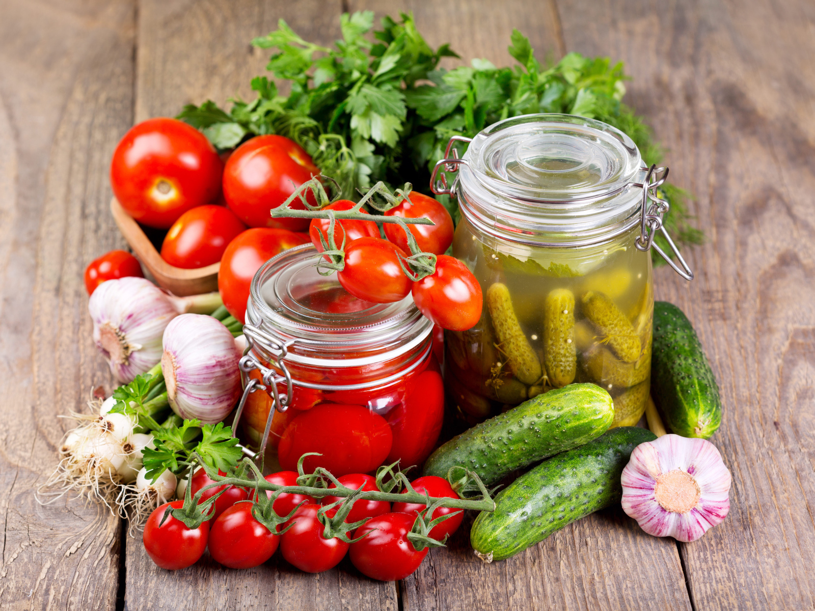 Консервированные помидоры и огурцы на столе со свежими овощами и зеленью 