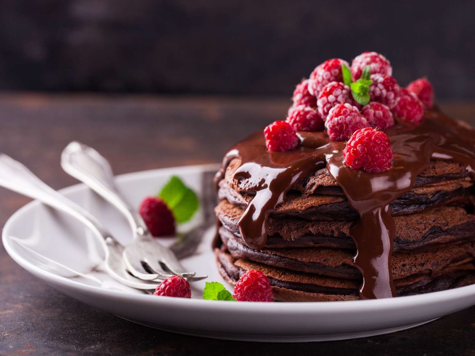 Шоколадные оладьи на тарелке с шоколадом и ягодами малины 