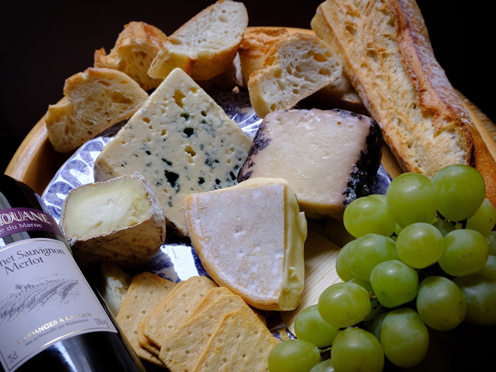 Разные виды твердого сыра на тарелке с белыми виноградом и вином