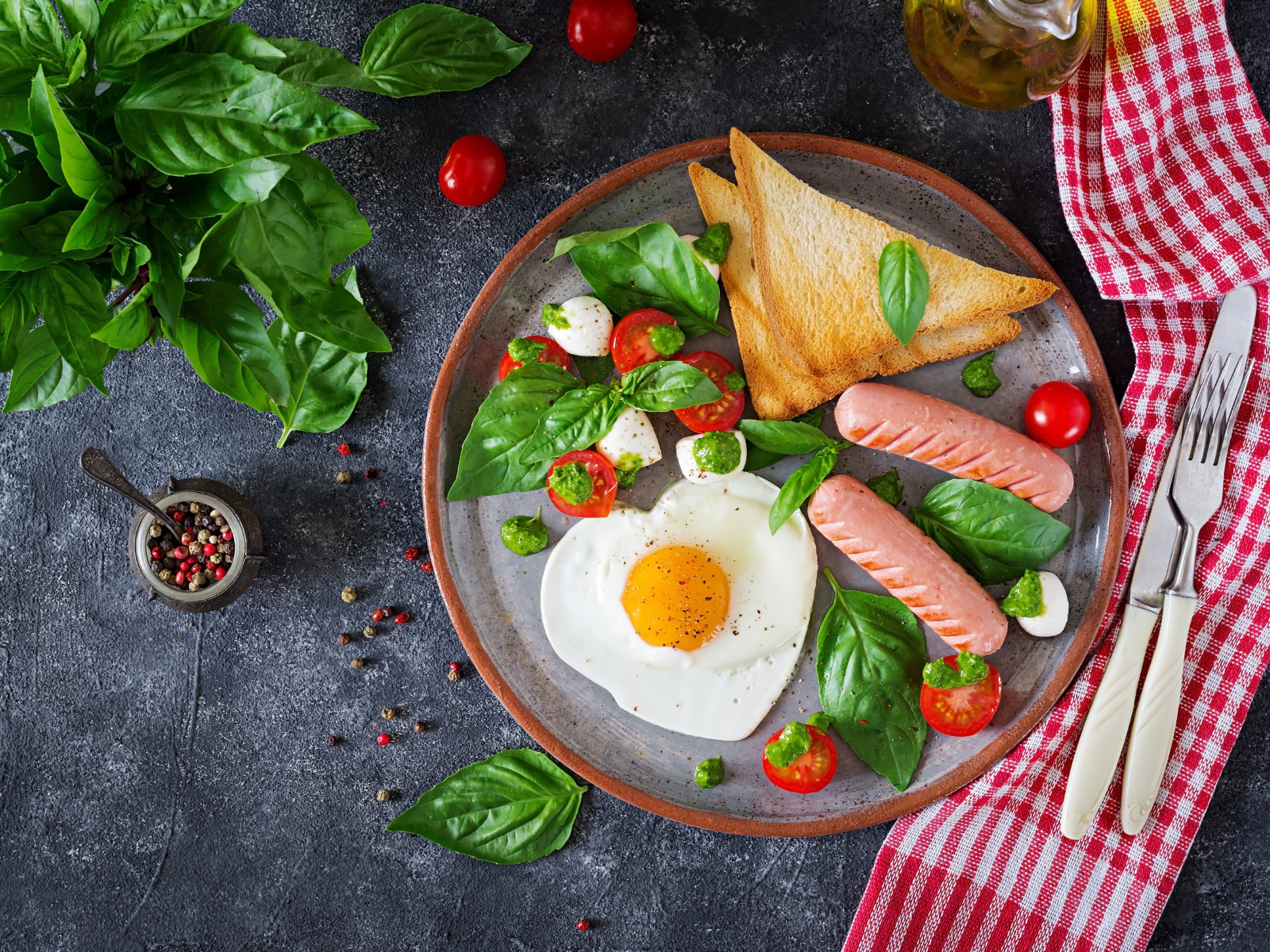 Яичница на тарелке с помидорами, гренками, сыром, сосисками и зеленью базилика