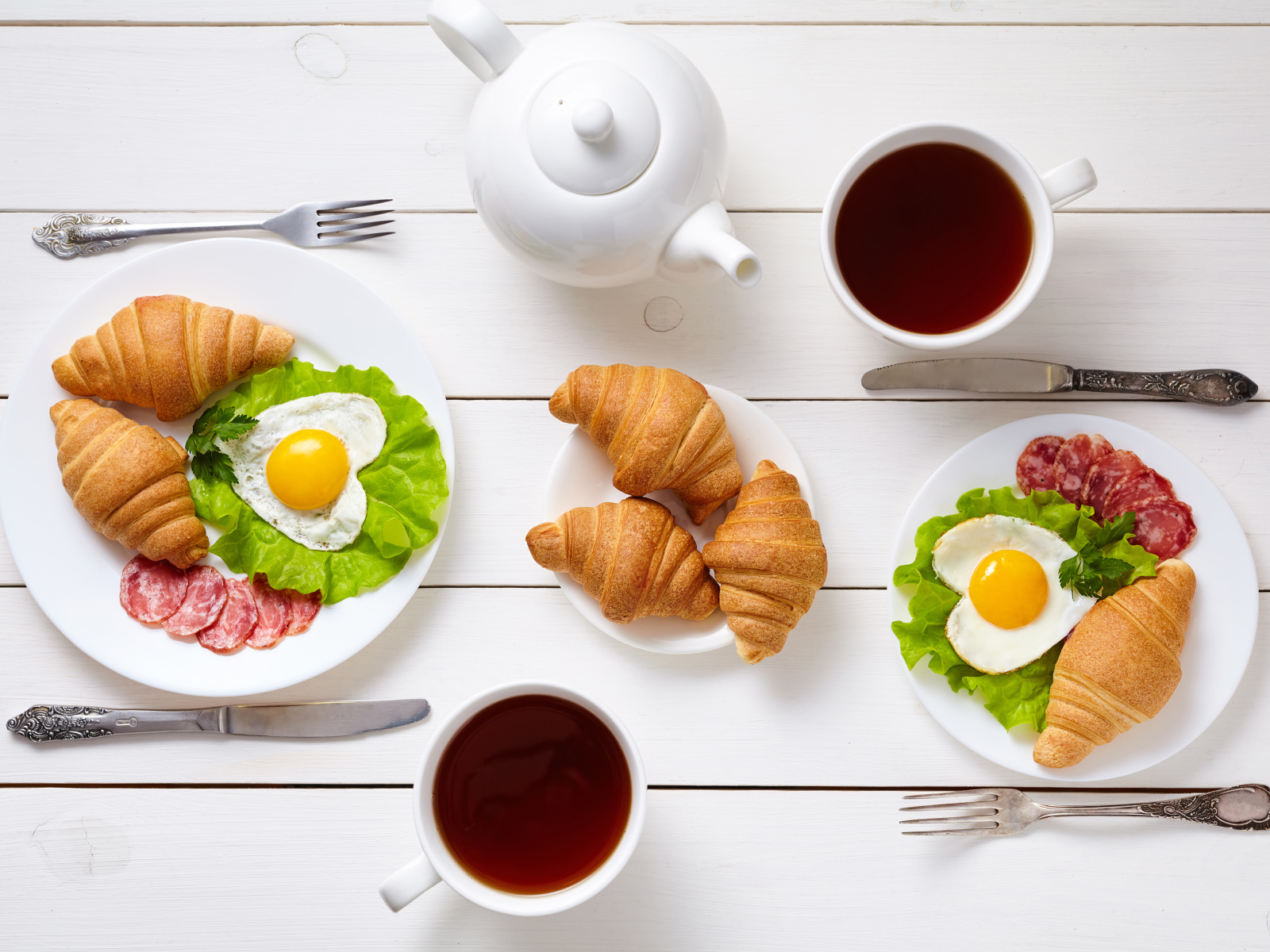 Яичница с колбасой и круассанами на столе чаем 