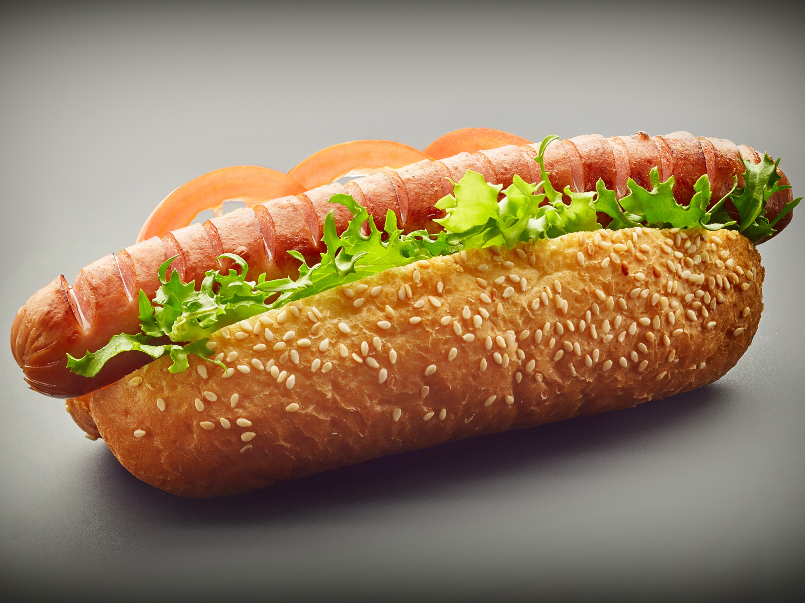 Хотдог с сосиской гриль и листьями салата на сером фоне