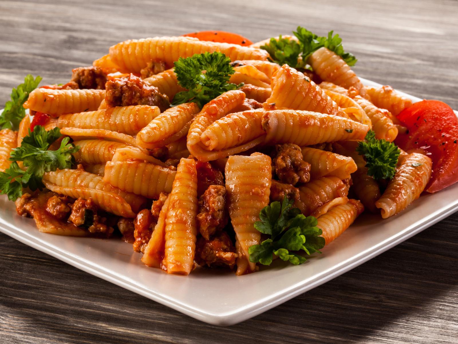 Паста с мясом, петрушкой и помидорами на белой тарелке