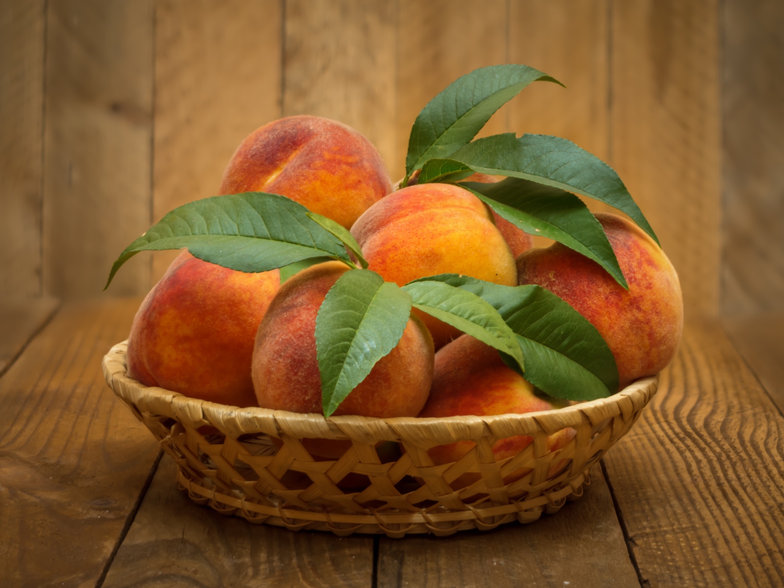 Корзинка персиков с зелеными листьями на столе