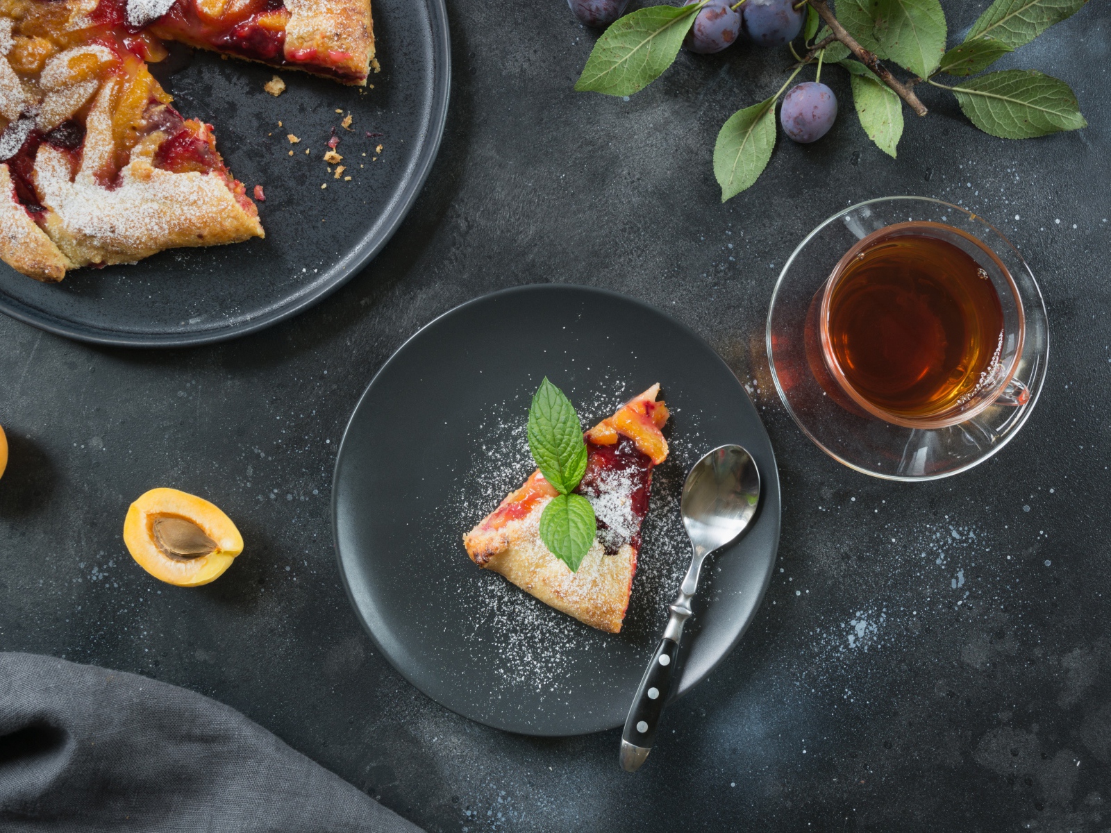 Кусок пирога с сахарной пудрой и абрикосами и сливами на столе с чаем 