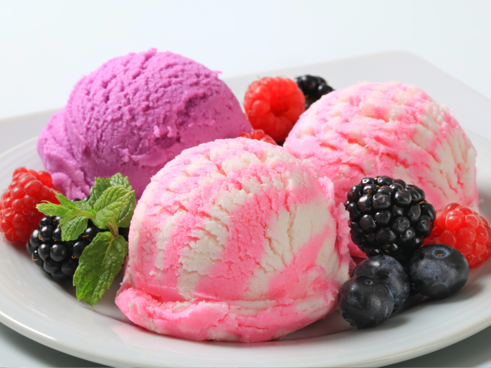 Шарики фруктового мороженого на белой тарелке с ягодами