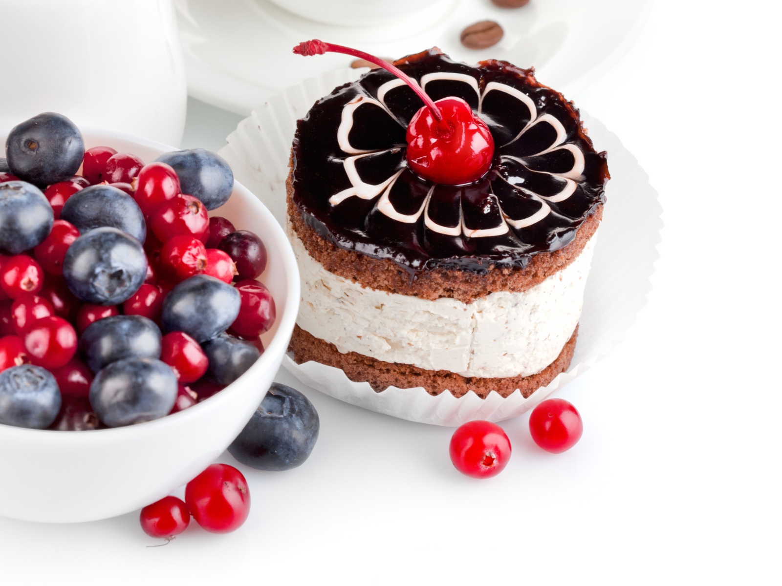 Пирожное с вишней на белом фоне с ягодами черники и клюквы