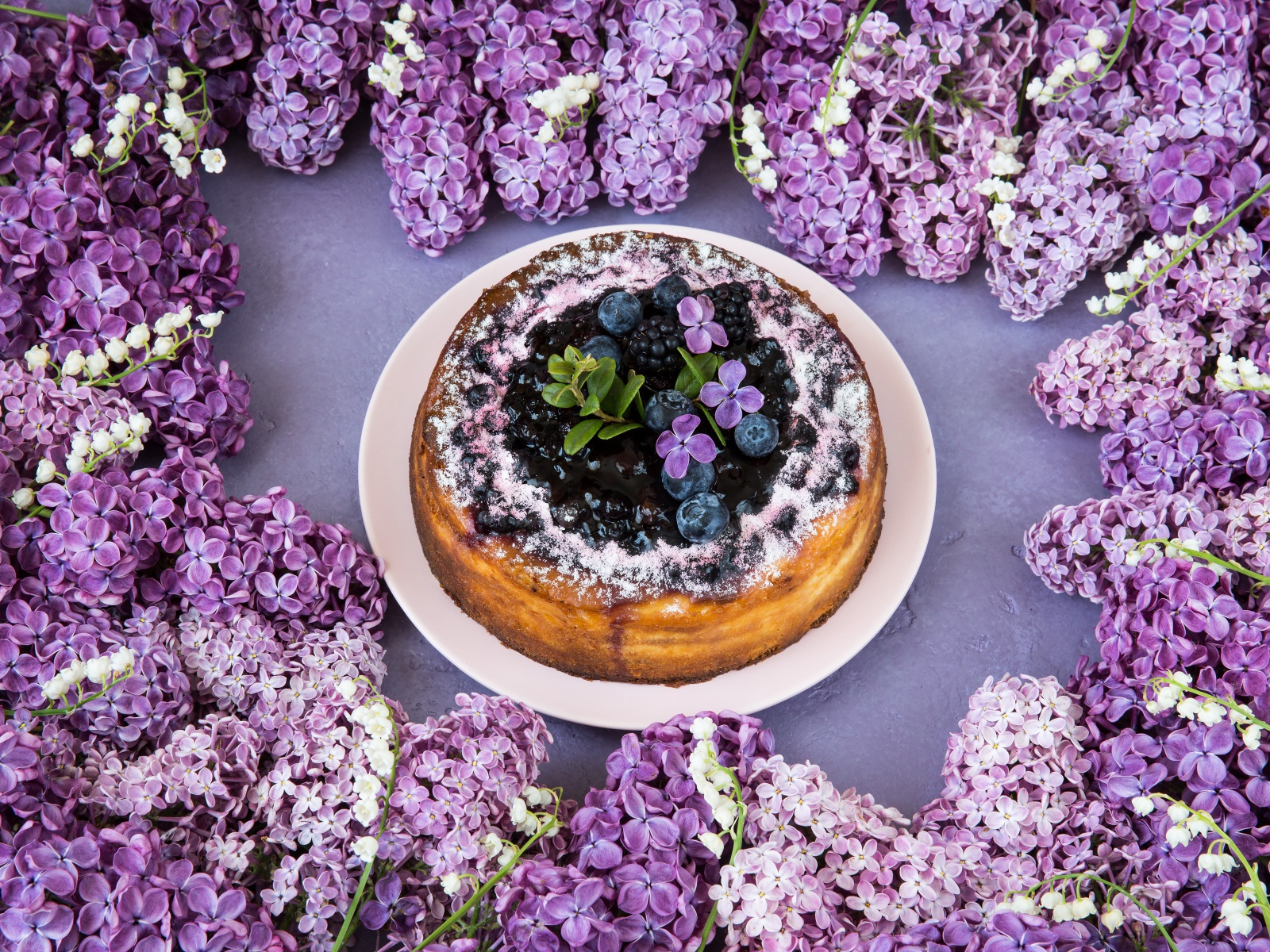 Аппетитный пирог с ягодами на столе с цветами сирени