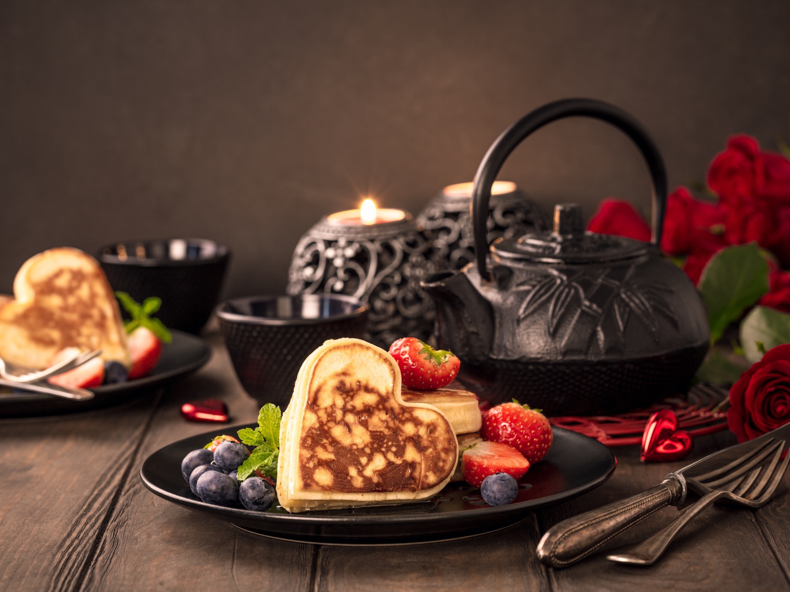 Оладьи в форме сердца с ягодами черники и клубники на столе с чаем и свечами