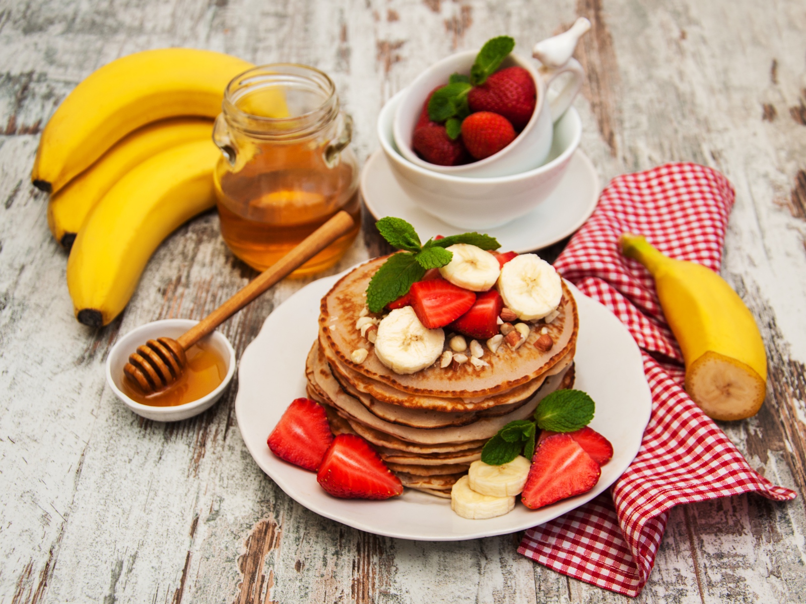 Оладьи с бананами и клубникой на столе с медом