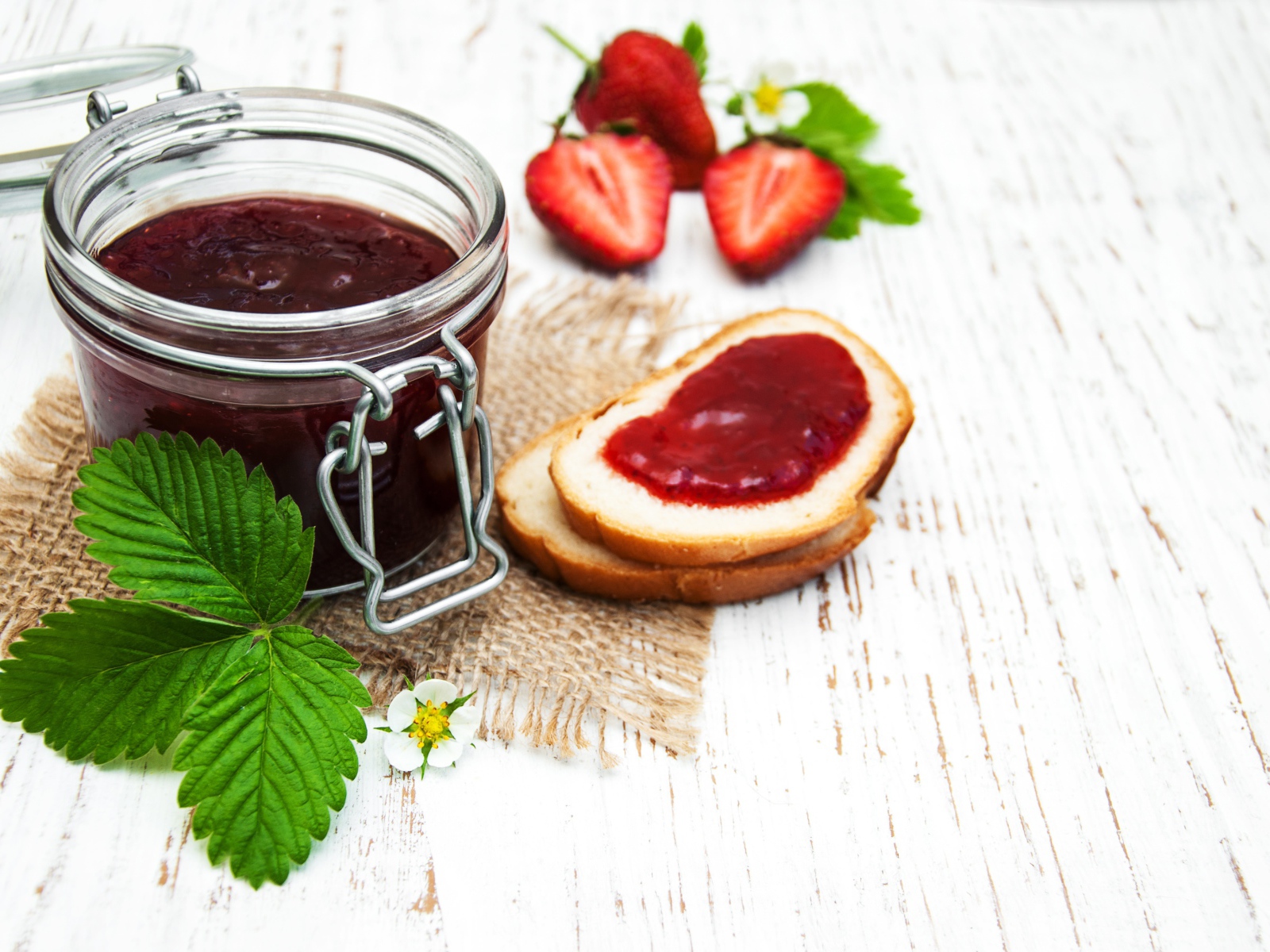 Банка клубничного джема на столе с батоном