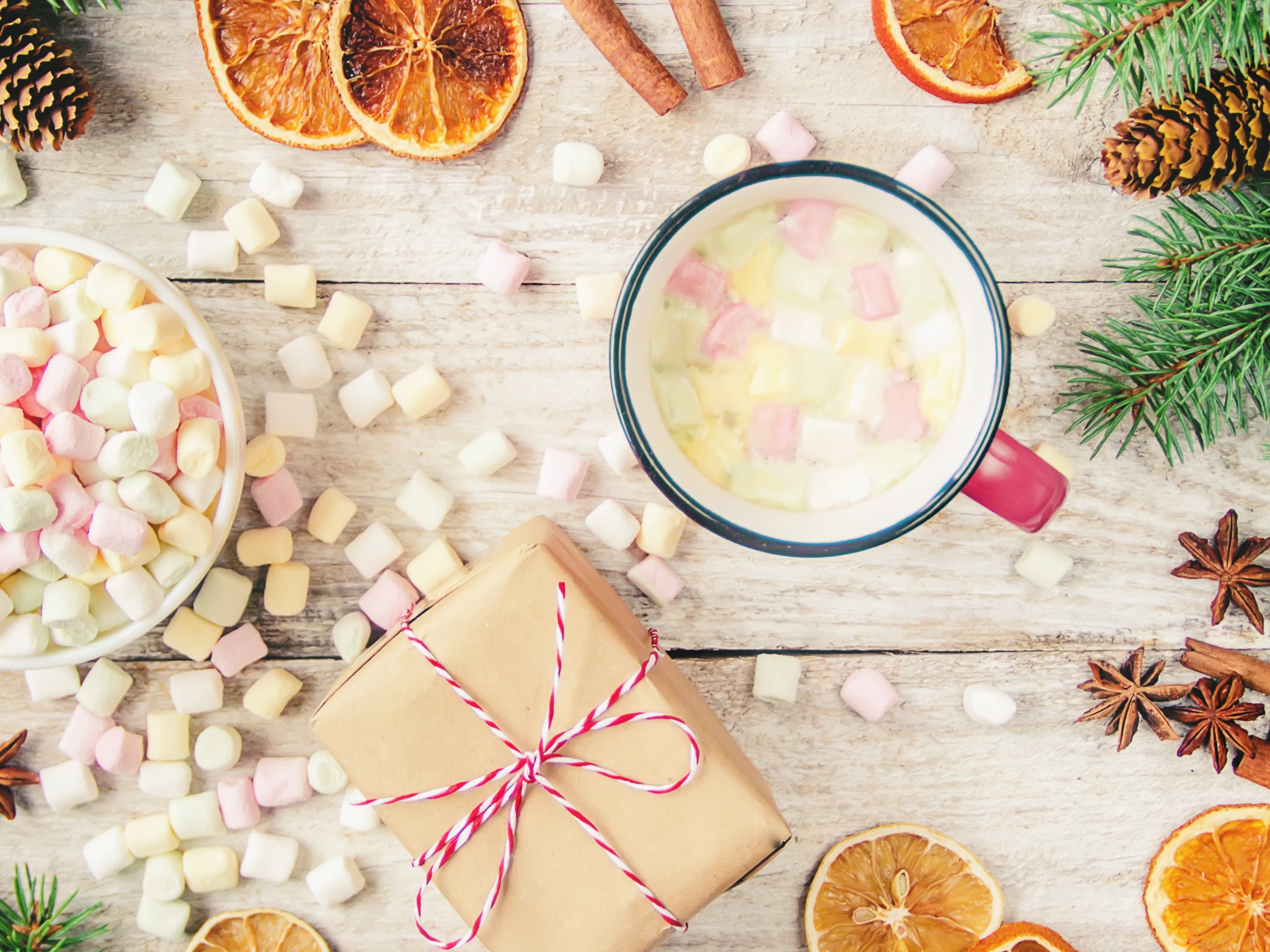 Кружка горячего напитка на столе с маршмеллоу, пряностями и подарком