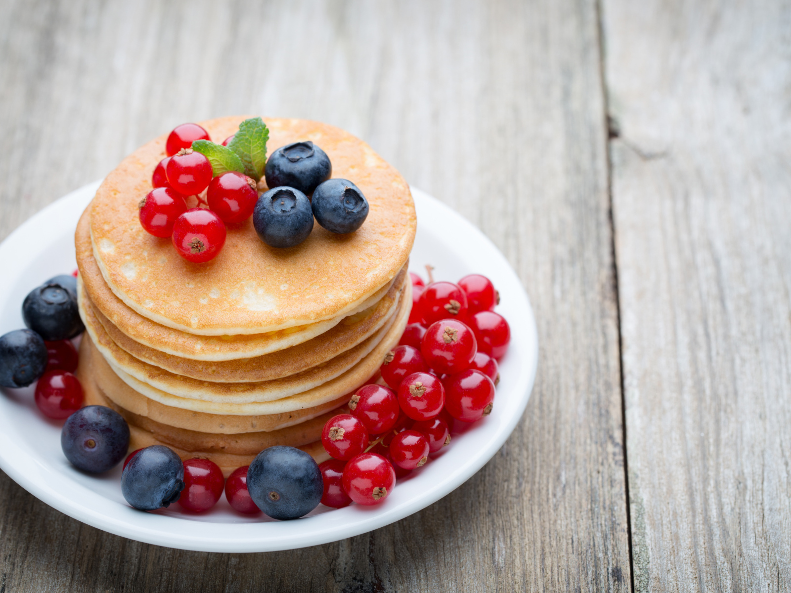 Вкусные оладьи на тарелке с ягодами красной смородины и черники